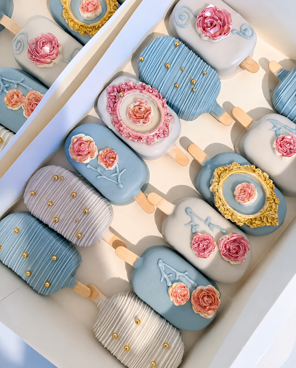 Dusty blue and white cakesicles with pink roses and gold accents
